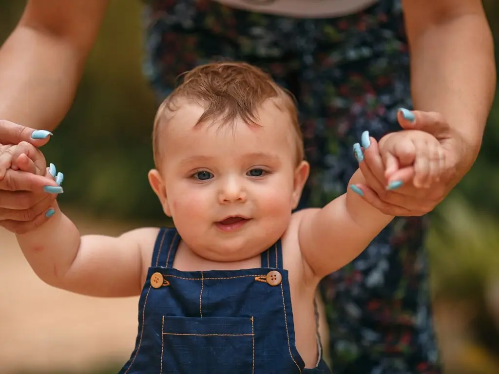 Bir yetişkinin elinden tutarak ilk adımlarını atan bebek